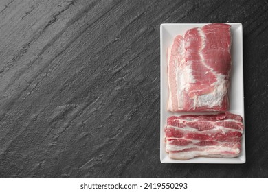 Pieces of raw pork belly on black textured table, top view. Space for text