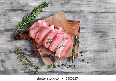 Pieces of raw pork steak with spices and herbs rosemary, thyme, basil, salt and pepper on a bright white wooden background in rustic style, top view