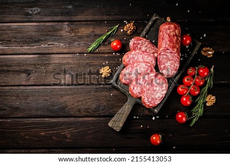Pieces of salami sausage on a cutting board with cherry tomatoes and rosemary. On a wooden background. High quality photo