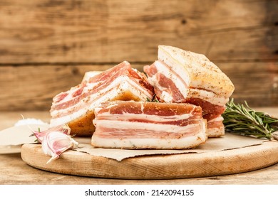 Pieces Of Salty High-fat Meat Cooked With Spices. Salo, Bacon, Lard, Silverside, Gammon. Garlic, Fresh Rosemary, Spices. Hard Light, Dark Shadow, Wooden Background, Copy Space