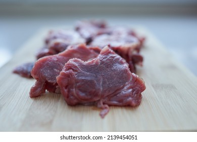 Pieces of sliced meat on a wooden chopping board close-up.                              