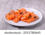 Pieces of smoked trout fillet with capers on a ceramic plate on a grey background