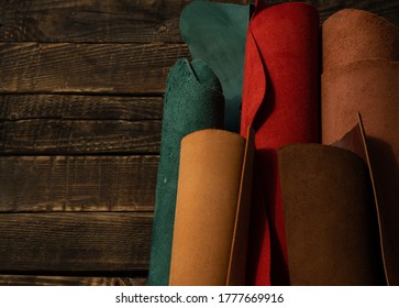 Pieces Of Tanned Leather On A Wooden Background. Leather Crafts Or Leather Work. Pieces Of Red, Cognac, Green, Red, Orange Leather On A Wooden Table. 