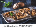 Pieces of tart, quiche with caramelized mushrooms, red onions and parsley on a dark background