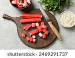 Pieces of tasty crab sticks, knife, sauce and parsley on gray textured table, flat lay