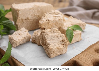 Pieces of tasty halva and mint leaves on table, closeup