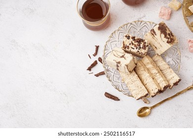 Pieces of tasty marble halva and glass with Turkish tea on white background