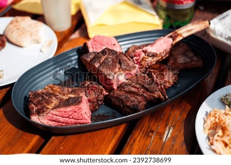 pieces of tomahawk steak on serving plate placed on a wooden table, ready to be eaten