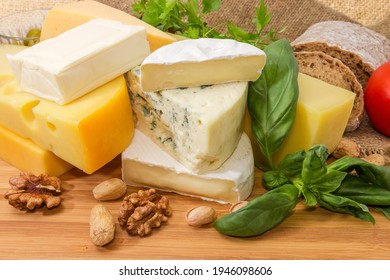 Pieces of various types of soft, semi-hard and blue cheese among the greens and nuts on a wooden surface - Shutterstock ID 1946098606