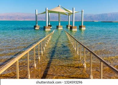 Pier on the beach over Dead Sea. Ein Bokek, Israel. Wooden path on yellow sand leaving in the distance of the dead sea. The path under the canopy in salt water. 