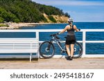 Pier in Orlowo Gdynia Poland. View from pier to Orlowski Cliff. Bike trip around Tri-City. Woman dressed in sportswear and white bike helmet standing backwards by bike on pier and looking at cliff.