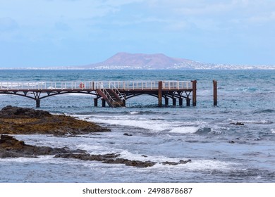 Pier over the ocean in Corralejo, Fuerteventura, Canary Islands, Spain. Pier is seen in front of a ocean. The pier is wooden and has a staircase leading up to it - Powered by Shutterstock