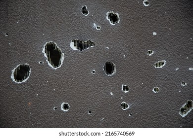 A pierced wall. Texture of a gray concrete background. Torn lattice. A shelled fence. Holes in the building. Black and white close-up photo. 