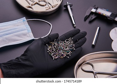 piercer master's hand in a medical black glove holds earrings. Around instrument for piercing and disinfection