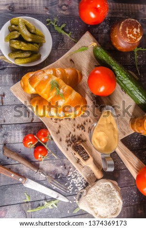 pies, loaf bread, dough on a wooden vintage cutting board old rustic, mustard sauce-dish, tomato, greens, black pepper gherkins, cucumbers, on the table top, side, bottom shot angle, fork and knife