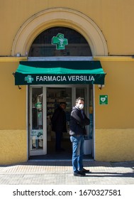 Pietrasanta, Lucca/Italy - Mar 11 2020 : Coronavirus In Italy, People Lined Up Waiting For Their Turn To Enter  The Pharmacy