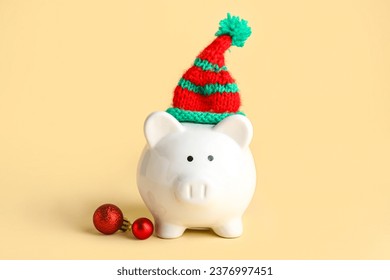 Piggy bank with Christmas hat and baubles on beige background