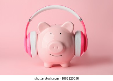 Piggy bank with headphones on color background