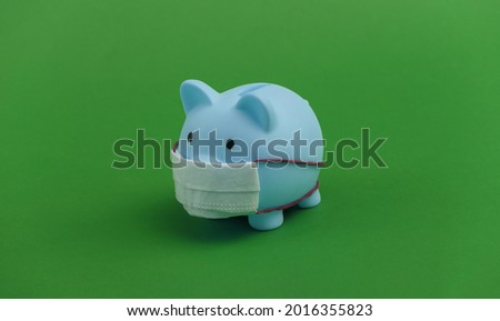 Piggy bank with medical mask on green background. Economic disease. Financial crisis. Covid-19 pandemic