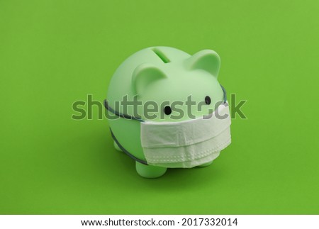 Piggy bank with medical mask on green background. Economic disease. Financial crisis. Covid-19 pandemic