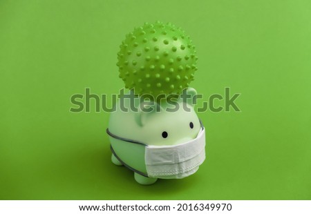 Piggy bank in medical mask with virus strain model on green background. Covid-19 pandemic