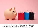 Piggy bank with Miniature shopping bags on pink background. Black Friday, world shopping day, sale