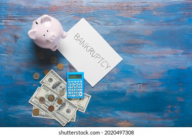 Piggy Bank With Money, Calculator And Paper Sheet With Word BANKRUPTCY On Color Wooden Background