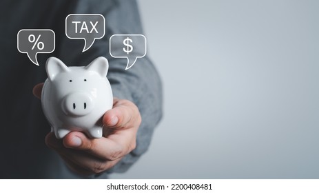 Piggy Bank Property Tax, Local Development Tax Concept. Word Tax, Man Holding Piggy Bank With Money,tax And Percent Icon. US Dollar Bags On A Table, Depicts Ad Valorem Tax On Value Of A Property.