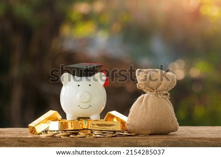 Piggy bank put on the gold bar and coin and money bag with saves with wear graduation cap put on the wood on bokeh sunlight background in the public park, Planning for education in the future concept.
