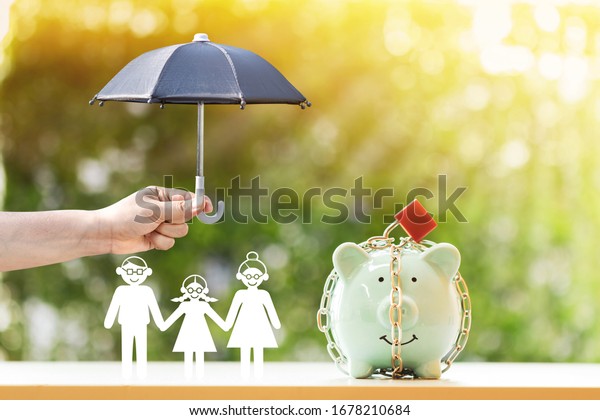 Piggy bank with security and lock and family and\
woman hand hold the black umbrella for protect on sunlight in the\
public park, to prevent for asset and saving money for buy health\
insurance concept.