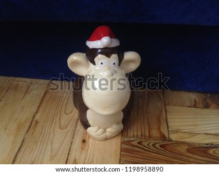 Piggy bank in the shape of a monkey in Santa's hat on the background of parquet and blue bedside table