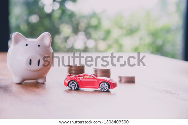 Piggy bank with sport car model on\
wooden floor for money saving or money assurance\
concept