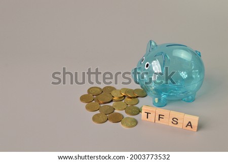 Piggy bank, stack of coins and wooden blocks with text TFSA stands for Tax-Free Savings Account
