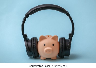 Piggy bank with stereo headphones listening to music on blue background