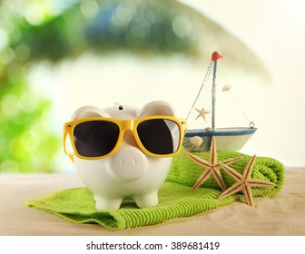 Piggy Bank With Towel And Sunglasses On A Sand. Holiday Money Concept