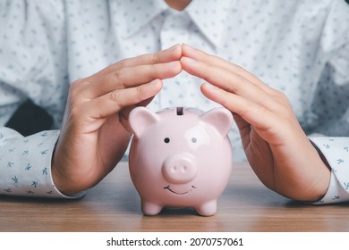 Piggy bank under hands in gesture of protection on wooden desk, saving, charity,  fundrasing community care, superannuation, financial crisis concept