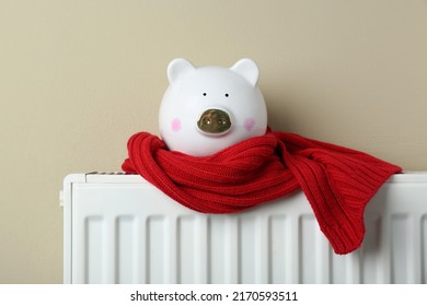 Piggy bank wrapped in scarf on heating radiator against beige background