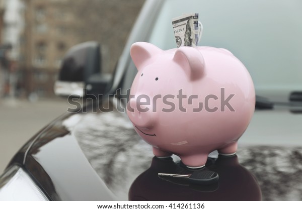 Piggy money box with cash and key on car bonnet at\
the street