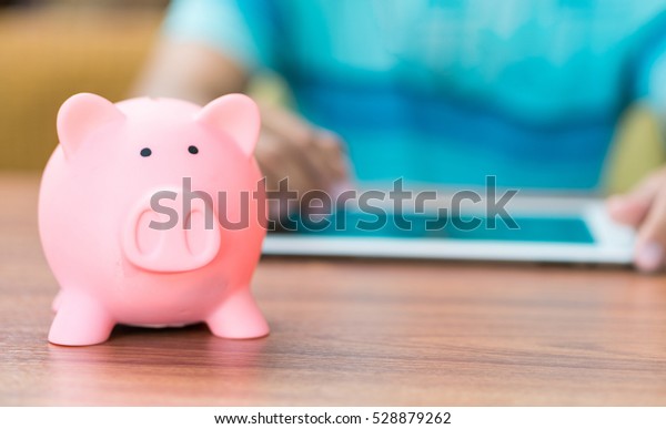 piggy saving bank with man working\
with tablet computer background, copy space on Right\
side.