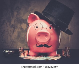 Piggybank in glasses and hat with pile of coins and banknotes  - Shutterstock ID 183282269