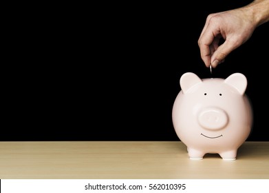 Piggybank on wooden table. A hand putting a coin into a piggy bank.