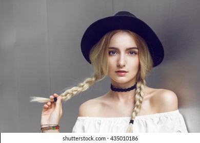 Pigtails. Close up of beautiful young blonde woman with black hat. Her hair is tied in two big ponytails. Around neck she has black choker.
					Professional make-up, hair style and styling.
					