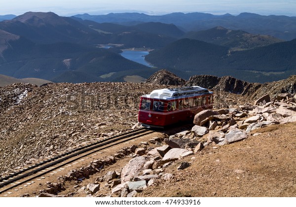 Pikes Peak Cog Railway car leaving the top of\
Pikes Peak mountain top in Colorado on sunny summer morning with\
mountains and lake in\
distance