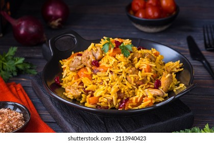 Pilaf, a dish of rice, chicken, carrots with spices and dried cranberries on a black plate on a dark wooden background. Eastern cuisine.