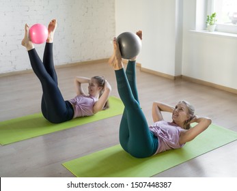 Pilates Abs Exercise With Small Fit Ball. Two Pretty Girls Lying On Mats And Raise Up Her Legs Doing Workout In Fitness Studio, Selective Focus. Gymnastics, Yoga, Group Training, Abdominal, Healthy