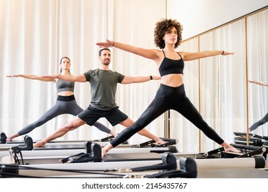Pilates class of diverse people doing standing yoga poses on reformer beds in a gym in a health and fitness concept - Shutterstock ID 2145435767