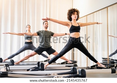 Pilates class of diverse people doing standing yoga poses on reformer beds in a gym in a health and fitness concept