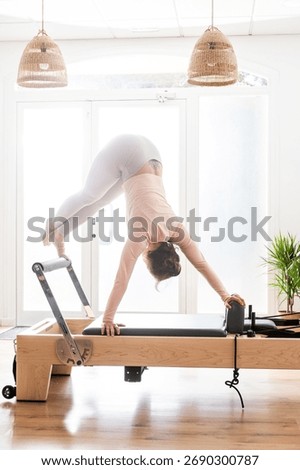 Pilates instructor is performing a jackknife exercise on a reformer in a bright studio, showcasing strength, flexibility, and control in pilates
