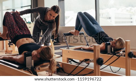 Pilates instructor training women at the gym. Two fitness women doing pilates workout on pilates equipment.