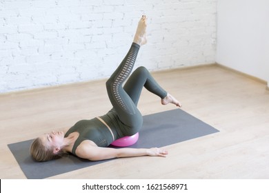 Pilates, leg arch exercise. Young caucasian fit woman doing work out with small pink fitness ball on the floor in loft studio indoor, selected focus. Wellness, recovery, rehabilitation, prevention